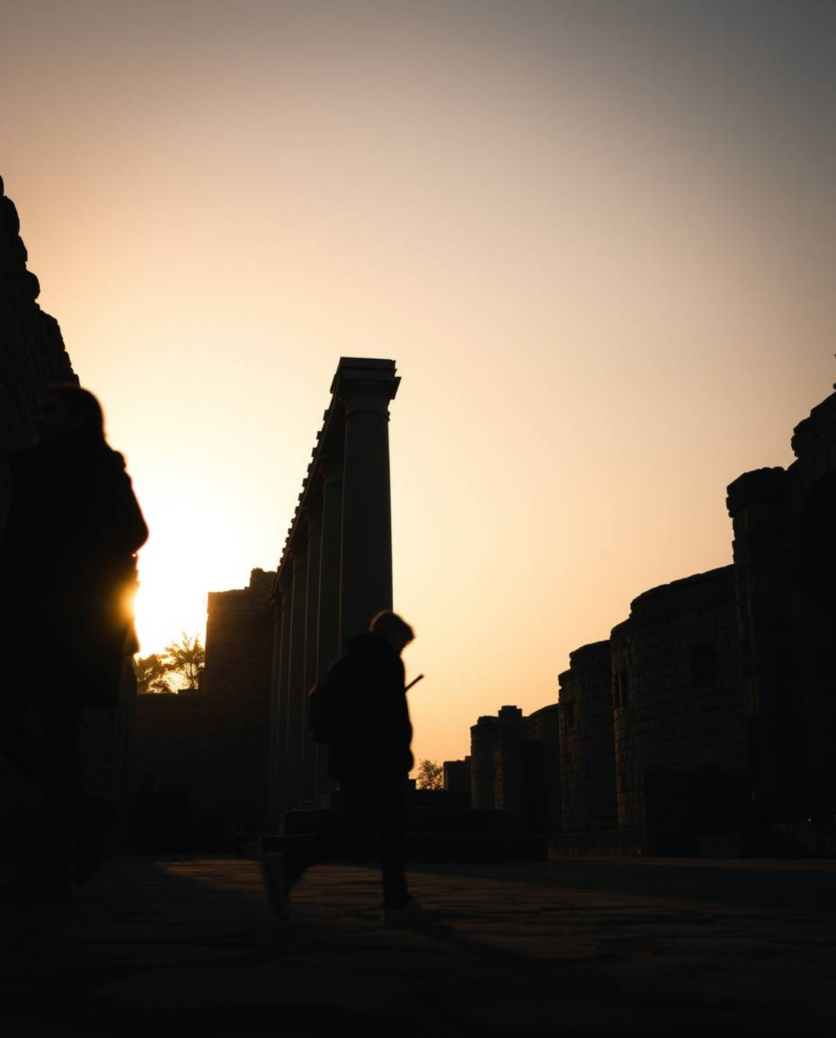 High-contrast, low-key lighting accentuates a cinematic street photography scene of ancient stone ruins at sunset. This image
