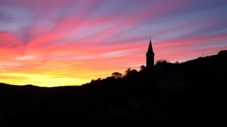 Experience the enchanting allure of a cozy village nestled in a valley, silhouetted against a vibrant sunset sky. The charmin