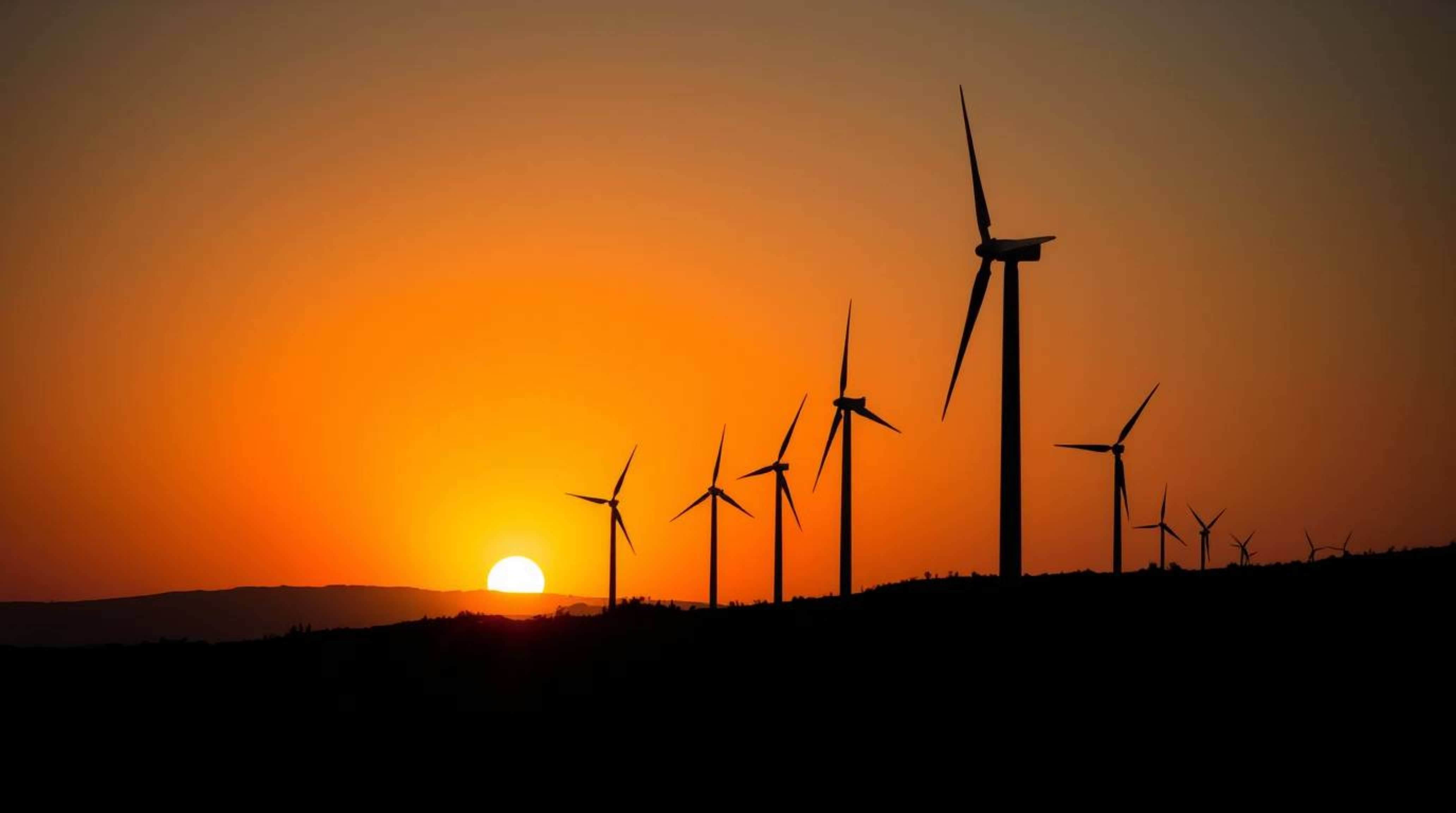 A captivating low-angle photograph showcasing a breathtaking sunset behind a row of wind turbines perched atop a hill.  The i