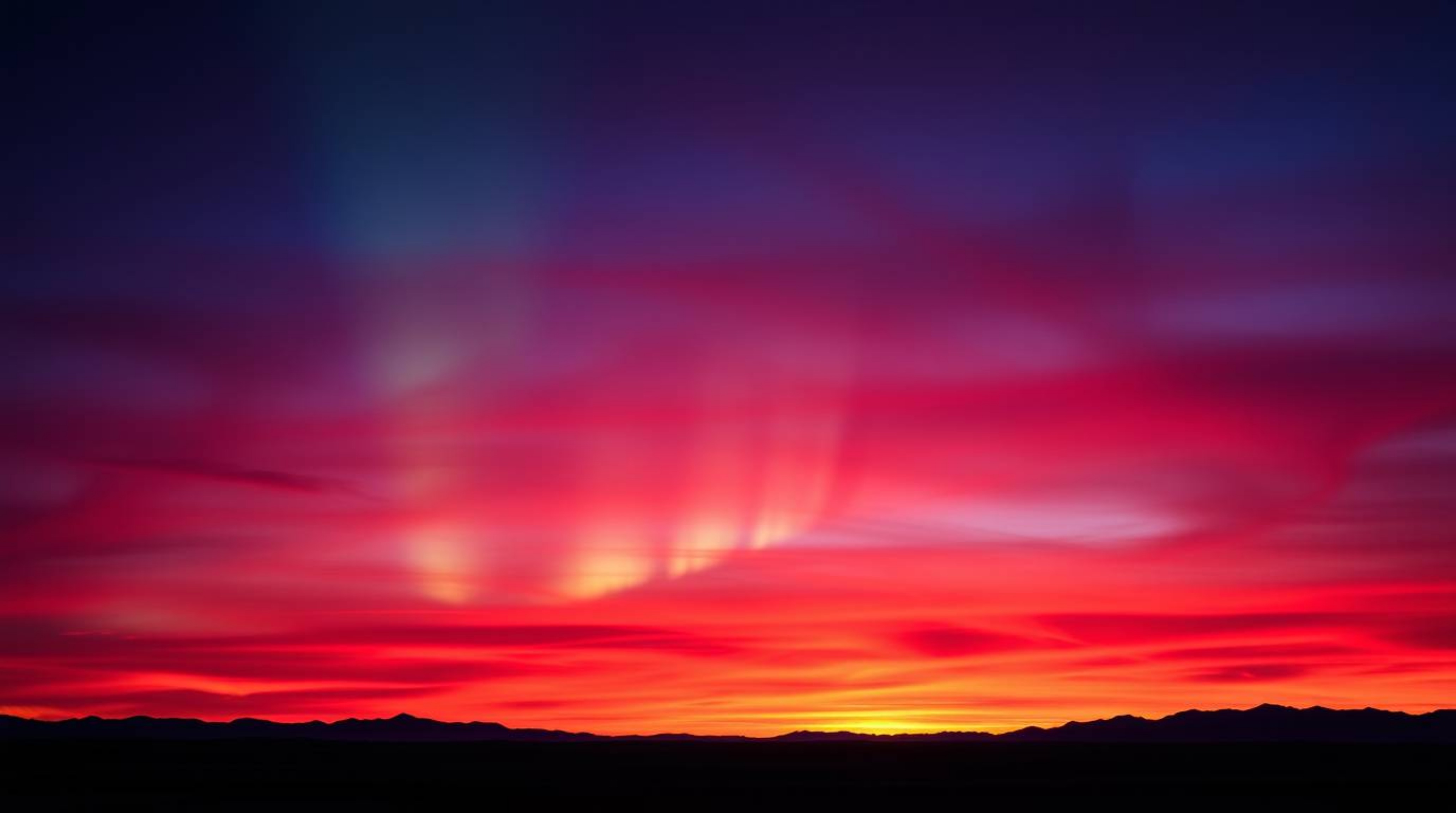 A captivating image showcasing rich burgundy and deep blue Northern Lights subtly emerging over a vibrant sunset sky.  This e