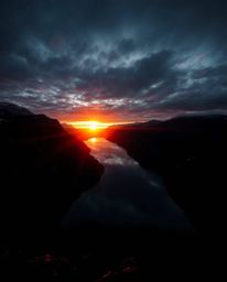 A high-angle perspective captures the reflection of a sunset in a glassy fjord, characterized by intense jet black and deep s