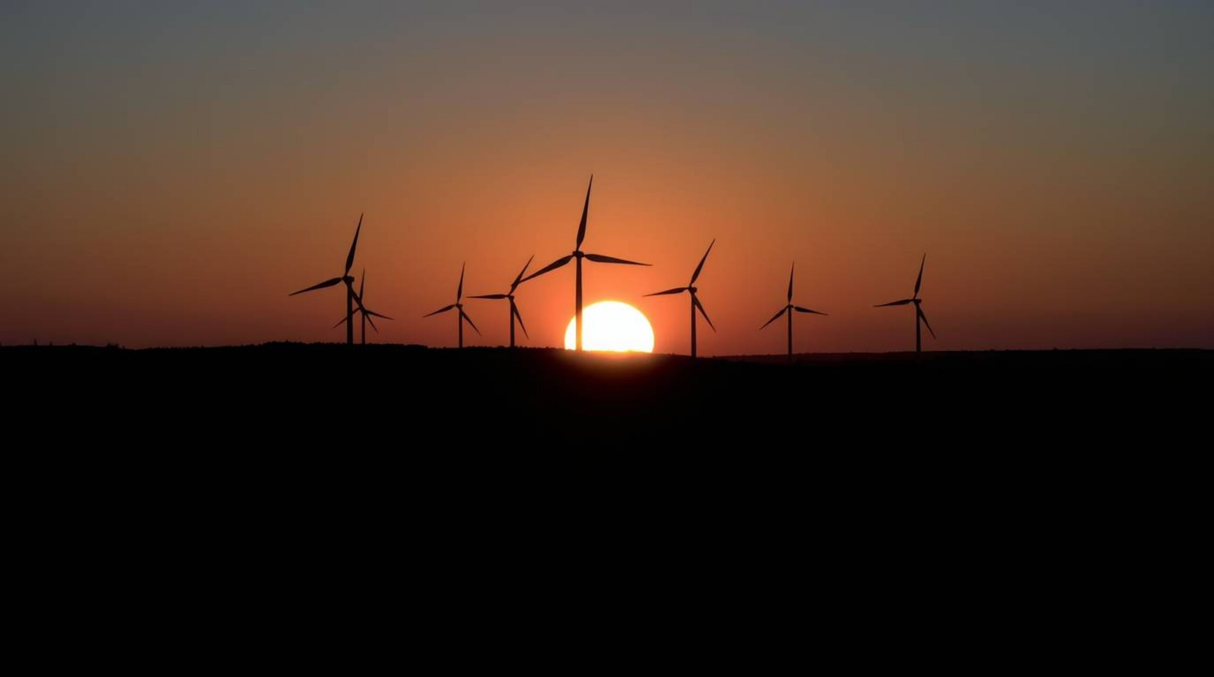 A captivating long exposure photograph showcases a dramatic split sunset behind a row of wind turbines.  The image features h