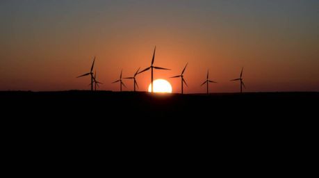 A captivating long exposure photograph showcases a dramatic split sunset behind a row of wind turbines.  The image features h