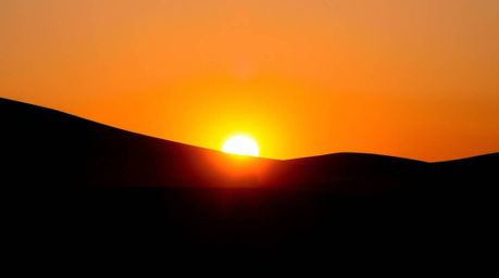 Capture the mesmerizing beauty of a desert sunset with golden dunes silhouetted against the horizon. This stunning image util