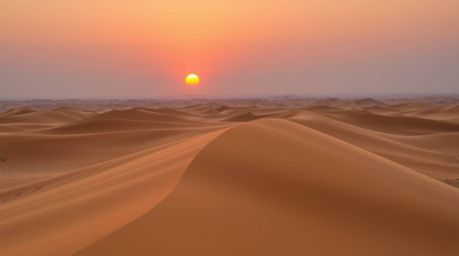 Experience the serene beauty of a desert sunset captured from a high-angle perspective. Witness the golden dunes bathed in ge