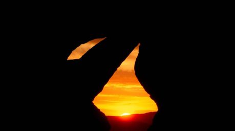 Experience the captivating beauty of a desert sunset framed by a natural rock arch. This image features high contrast and low