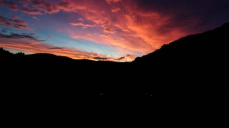 Discover a breathtaking image of a cozy village nestled in a valley, dramatically silhouetted against a vibrant, colorful sky