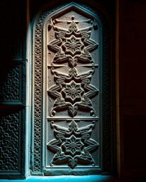 This photograph captures the beauty of Islamic geometric patterns carved in stone, illuminated by contrasting warm terracotta