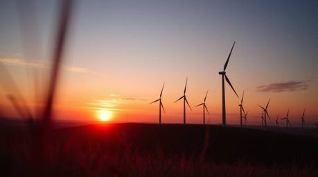 An extreme macro close-up shot captures a breathtaking sunset unfolding behind a row of wind turbines perched atop a hill. Th