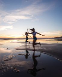 A dynamic, in-motion scene depicts a stunning sunset sky mirrored in the tidal pools on a beach. Captured during the warm gol