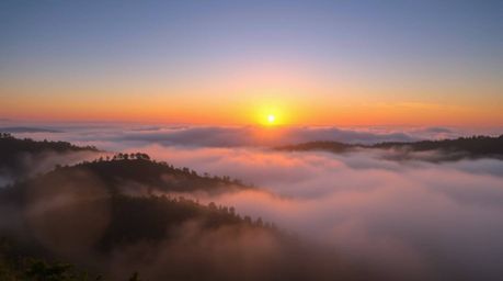 A breathtaking image showcasing radiant, fog-covered hills bathed in the warm golden light of sunset.  This stunning 16:9 lan