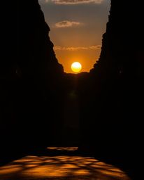 A creative light art piece featuring a sunset casting shadows through ancient stone ruins. The scene is characterized by its 