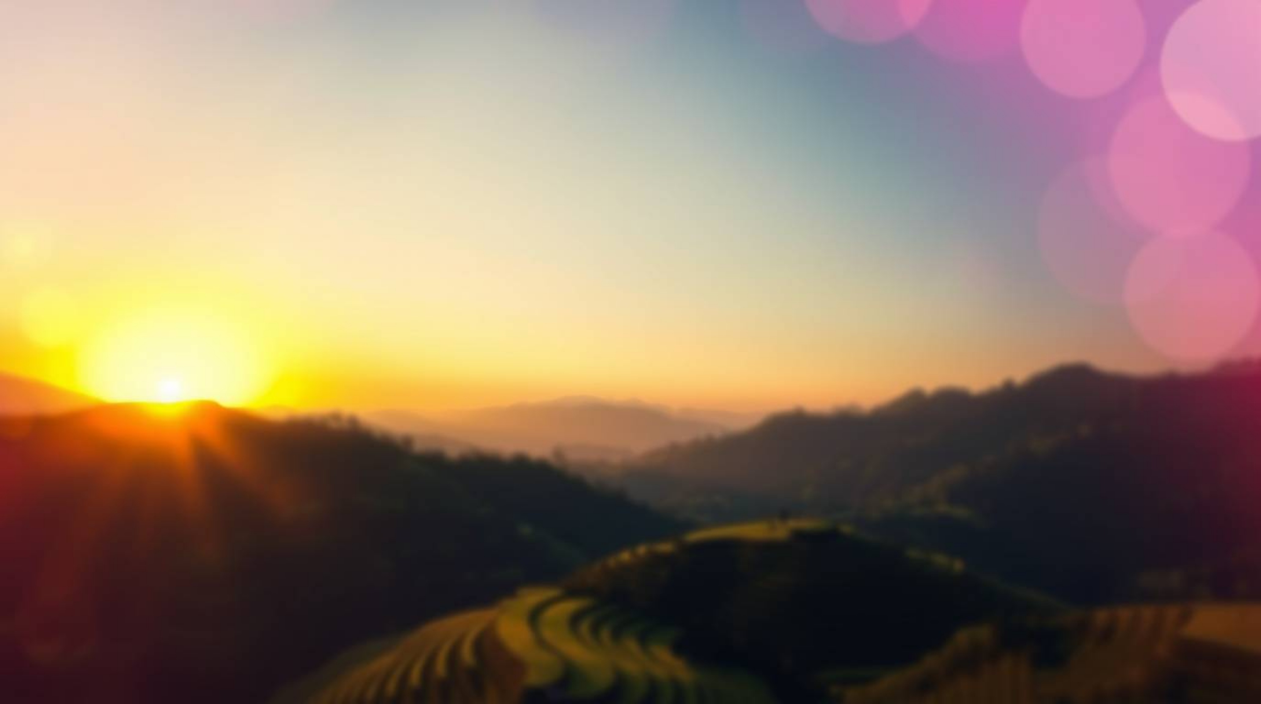 Experience the breathtaking beauty of a sunset casting its golden hues over lush rice terraces nestled in majestic mountains.