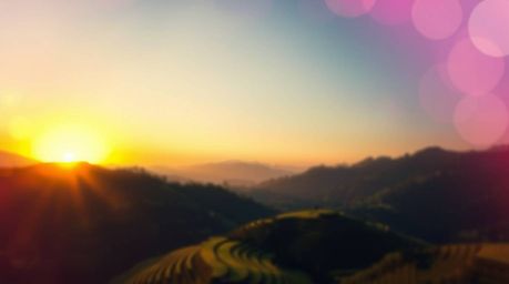 Experience the breathtaking beauty of a sunset casting its golden hues over lush rice terraces nestled in majestic mountains.