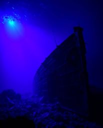This image showcases a dramatic underwater shipwreck scene, illuminated with high contrast, low key lighting and deep ultravi