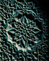 Explore the beauty of intricately carved Islamic geometric stone patterns in rich, deep teal hues. This high-contrast image s