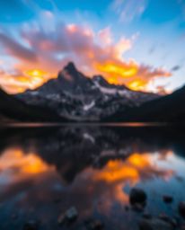 Long exposure photography captures the stunning reflections of fiery clouds in a mountain lake. The image features a beautifu