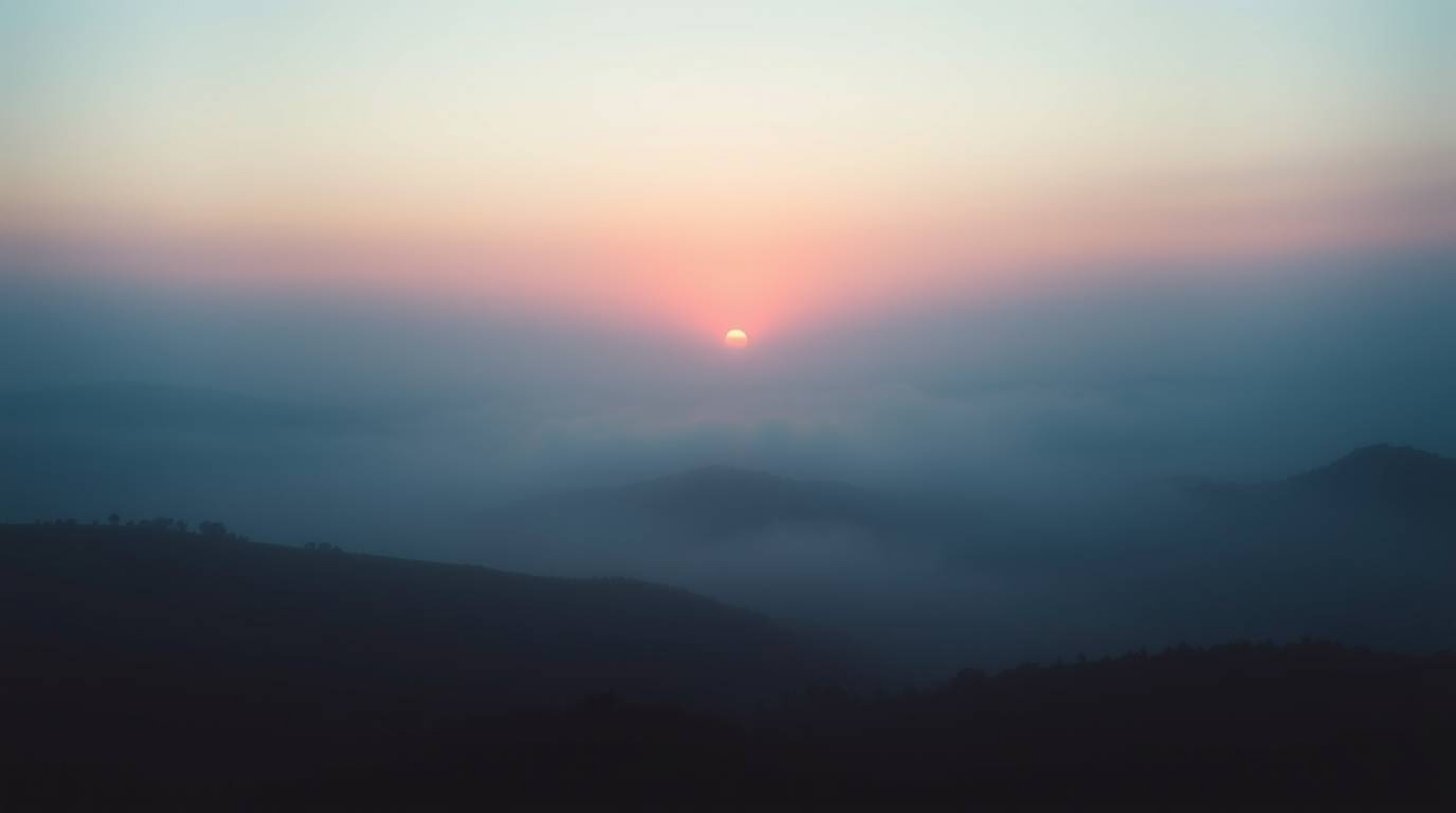 A breathtaking soft cinematic image capturing fog-covered hills bathed in the warm hues of sunset. The scene is rendered in c
