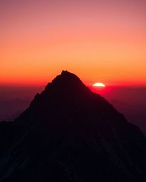 This is a high-contrast image capturing a sunset from a high alpine peak, illuminated with warm, low-key lighting. The scene 