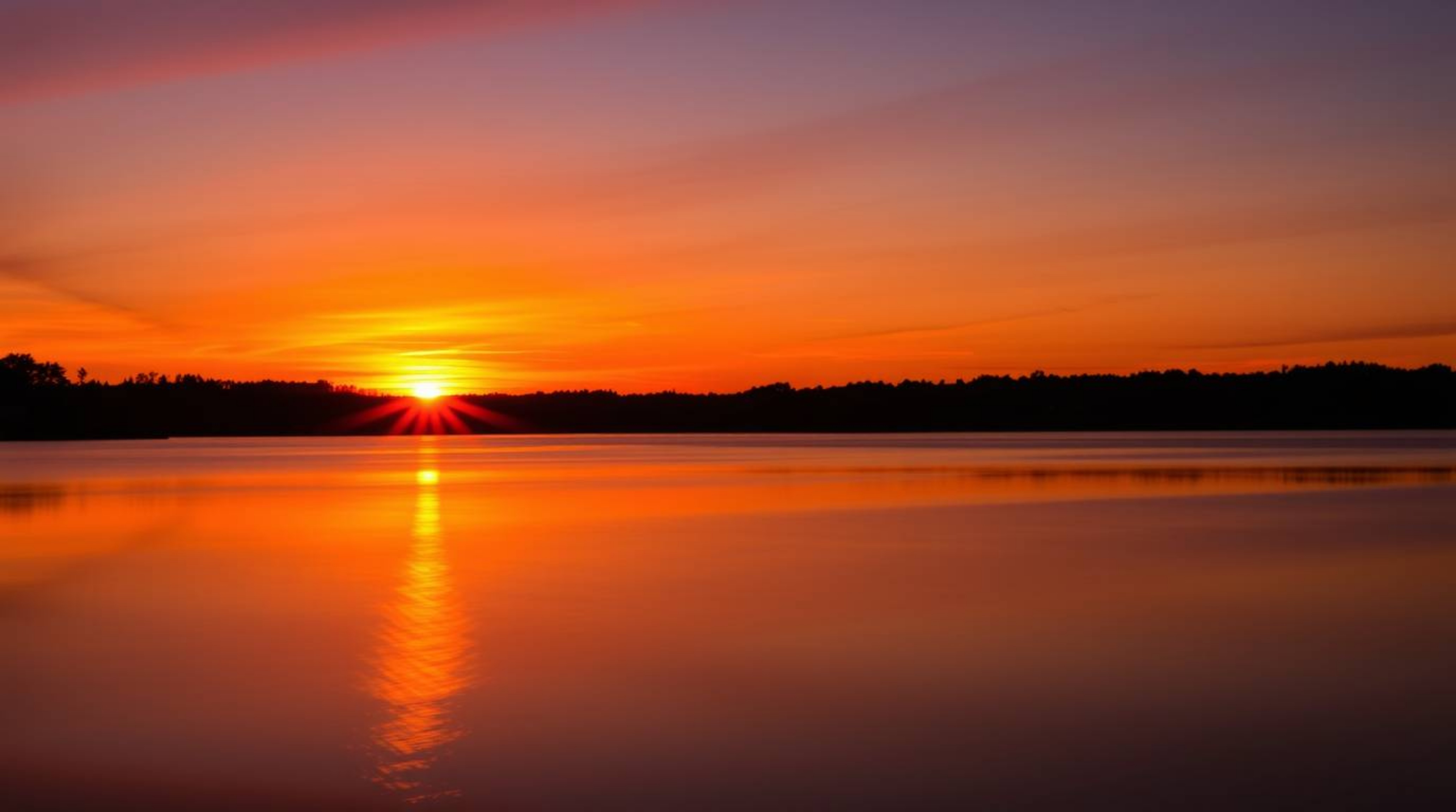 A captivating long-exposure photograph showcases a serene lake mirroring a vibrant sunset sky.  Silhouetted against the brigh