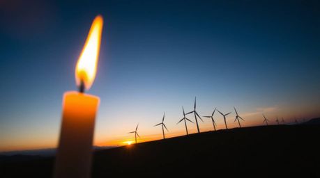 Experience the beauty of a sunset behind a row of wind turbines, captured from a high-angle perspective. Warm candlelight fli