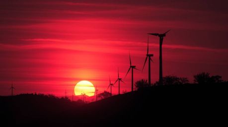 This surreal infrared image captures a creepy sunset looming behind wind turbines atop a hill. The dark tones and unsettling 