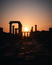 A cinematic sunset casts long shadows across ancient stone ruins, creating a mystic, dreamlike atmosphere. With gentle color 
