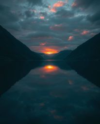 An image of a glassy fjord reflecting a sunset, illuminated by intense dramatic lighting. The scene is characterized by a str