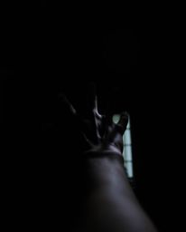A hand reaching towards a light source emerging from a dark and shadowy background creates an intense and dramatic visual. Th