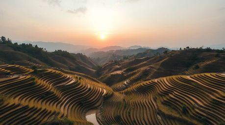 Experience a breathtaking overhead bird's-eye view of a serene sunset casting its warm glow over mountainous rice terraces. T