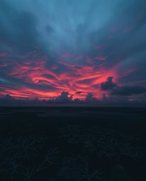 A moody image of a colorful sky over a coral reef at low tide, rendered in dark tones and low contrast. This piece is charact