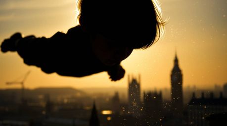 An extreme macro close-up reveals a silhouetted young boy, seemingly flying with pixie dust above a barely visible London. T