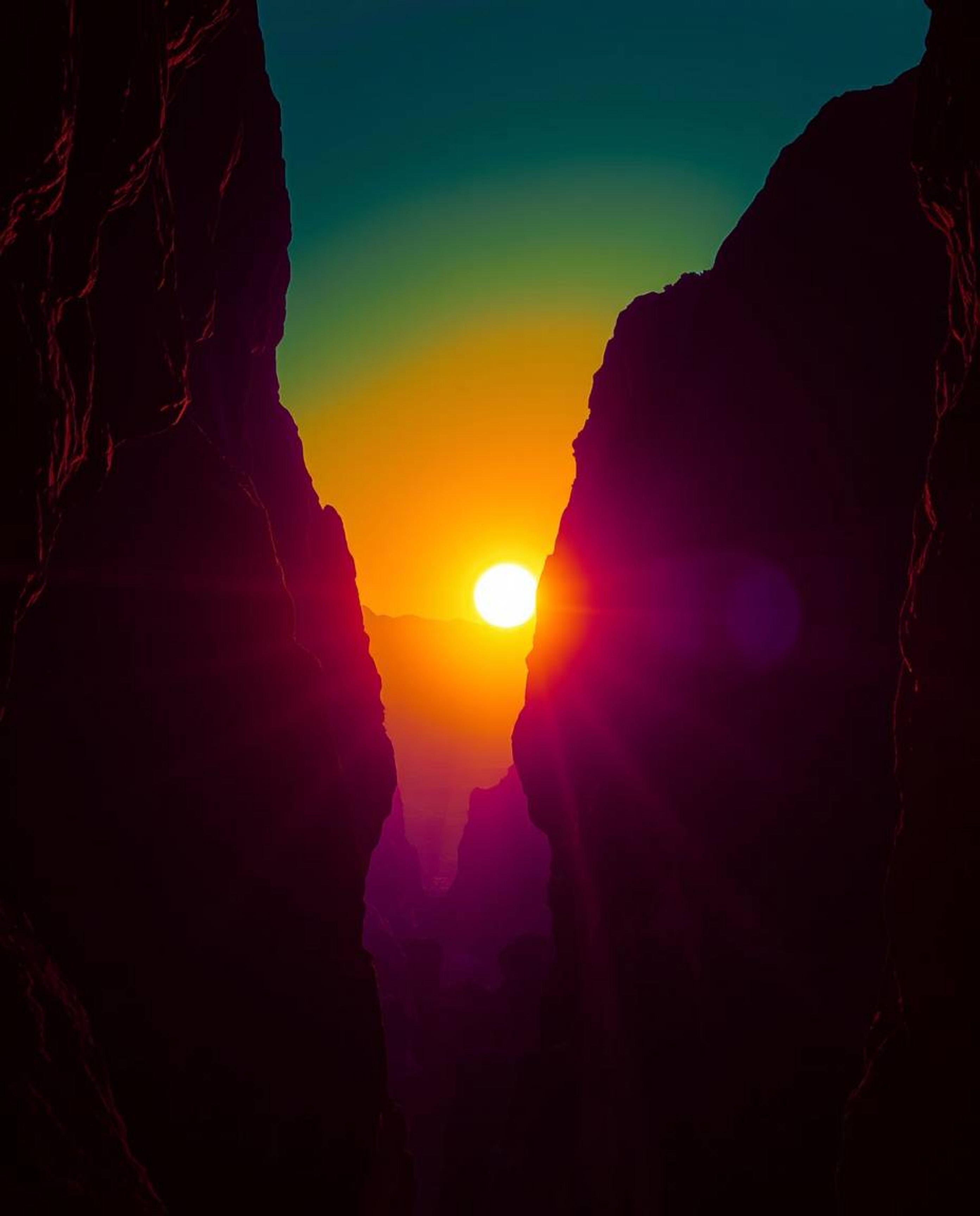 An intensely lit scene captures a sunset illuminating sandstone cliffs within a canyon, where the landscape is dominated by d