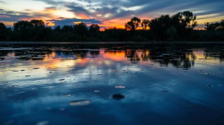 A serene image depicts a calm pond perfectly mirroring a vibrant sunset painted in blues, greens, and purples.  A gentle driz