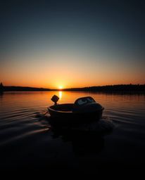 An intensely jet black image portrays an adorable, cute boat with charming features as it drifts on a lake at sunset. The sce