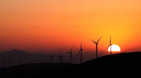 Capture the beauty of a smooth gradient sunset illuminating a row of wind turbines atop a hill. This scene showcases chiarosc