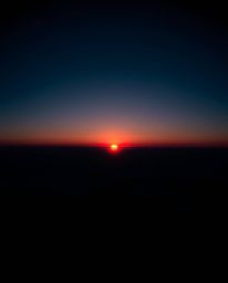 This is a high-contrast, low-key image capturing a sunset from a high alpine peak in a strong and moody style. The compositio