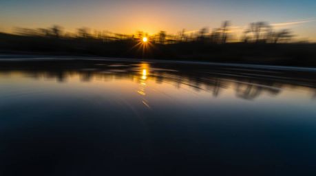 A breathtaking low-angle long-exposure photograph showcases a serene pond mirroring a vibrant sunset.  The image emphasizes t