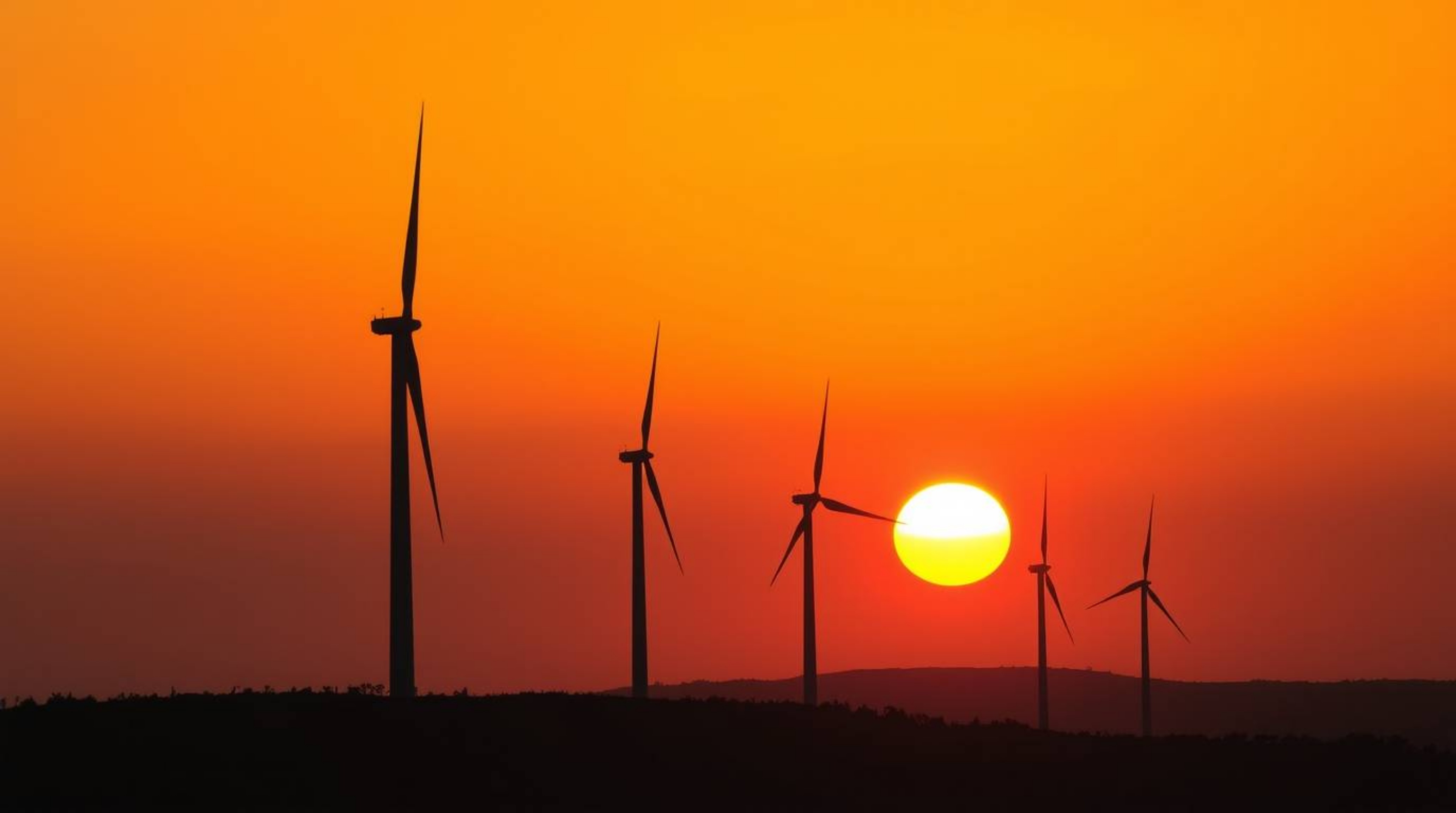 A captivating high-resolution stock photo showcasing a stunning sunset behind wind turbines perched atop a hill. This commerc