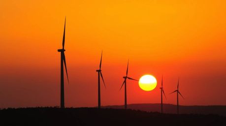 A captivating high-resolution stock photo showcasing a stunning sunset behind wind turbines perched atop a hill. This commerc