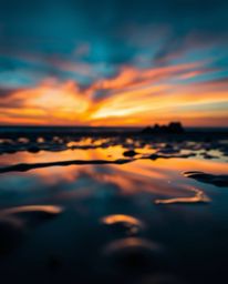 A rich, deep teal sunset sky is beautifully mirrored in the tranquil tidal pools of a beach, creating a stunning visual symph