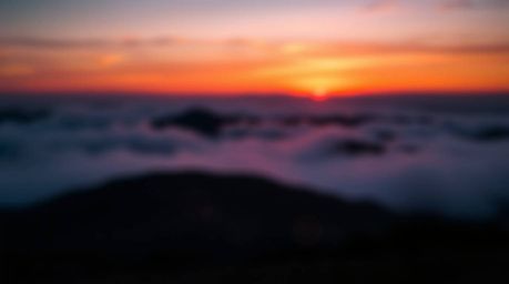 A breathtaking image captures the elegance of fog-covered hills at sunset.  Bioluminescent colors of rich burgundy and deep b