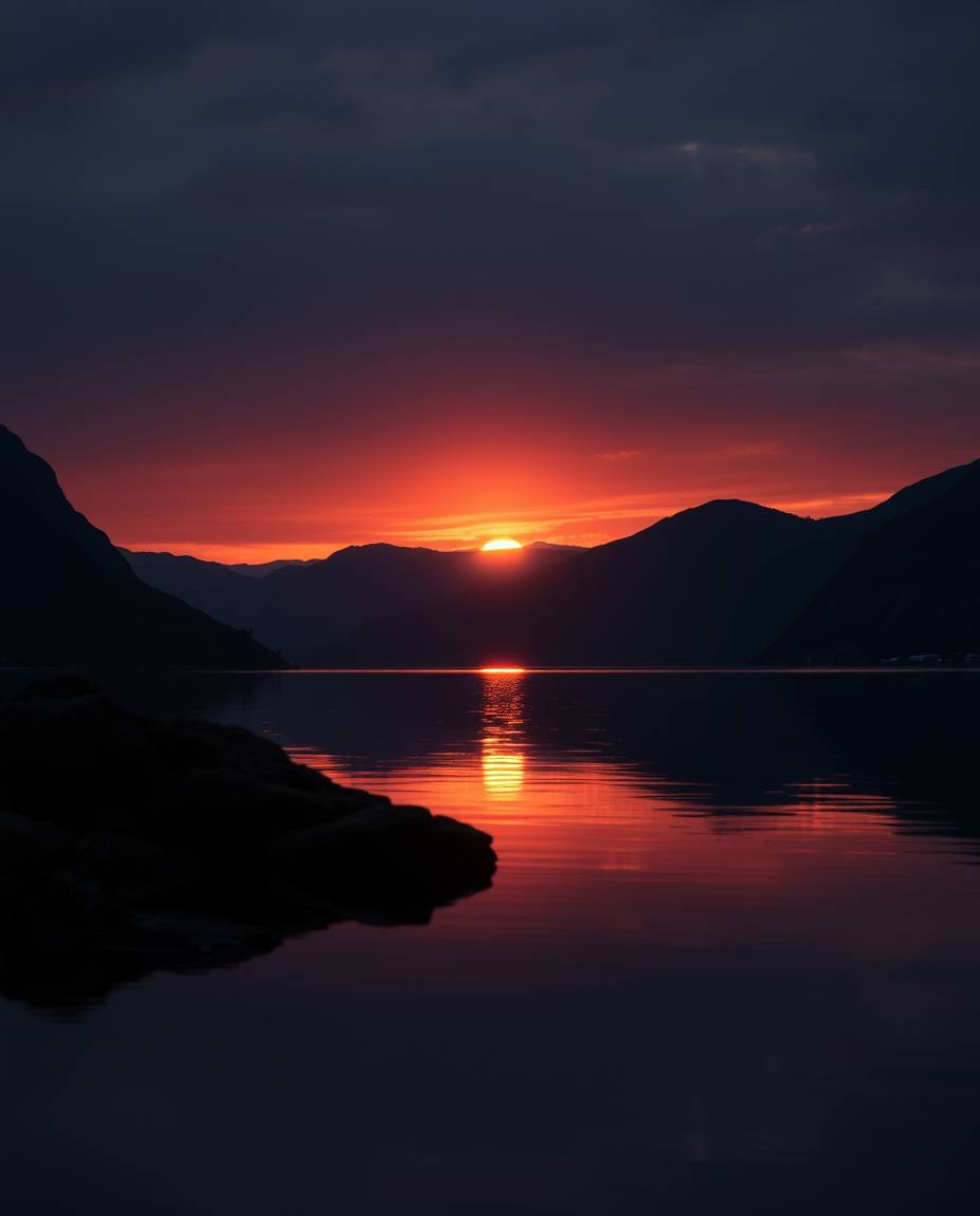 A fine art photograph captures a warm, slightly dark, and soft professional image of a sunset reflection in a glassy fjord. T