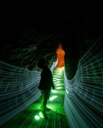 A captivating low-angle, long exposure photograph showcasing a child, silhouetted against glowing footsteps, gazing upwards i