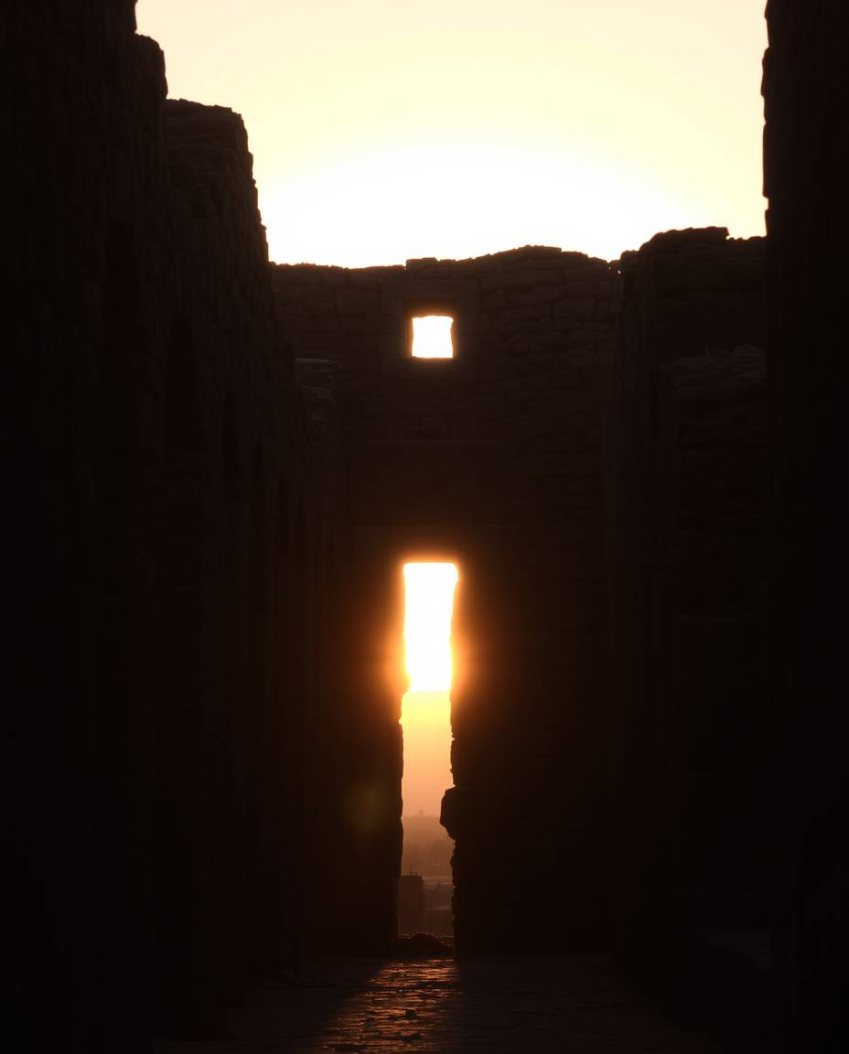 A scene of a sunset casting shadows through ancient stone ruins, characterized by natural earth tones. The composition featur