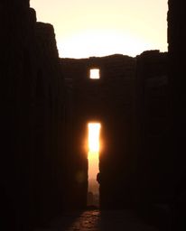 A scene of a sunset casting shadows through ancient stone ruins, characterized by natural earth tones. The composition featur