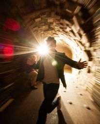 A figure is captured in dynamic motion, seemingly discovering a hidden underground library illuminated by a bright lens flare