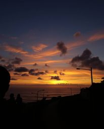 This piece of candid street photography captures a sunset sky over a winding coastal highway, employing contrasting chiaroscu