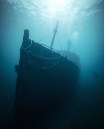 A stunning cinematic underwater photograph capturing the haunting beauty of a shipwreck illuminated by soft, diffused light. 