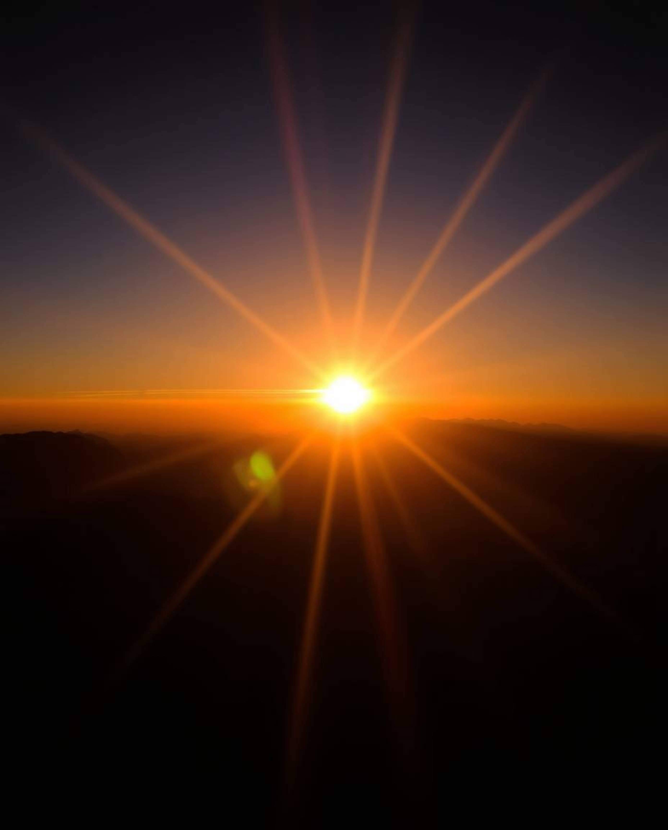 This is an intense photograph of a sunset from a high alpine peak, dominated by pure, jet black tones and deep shadows. The d